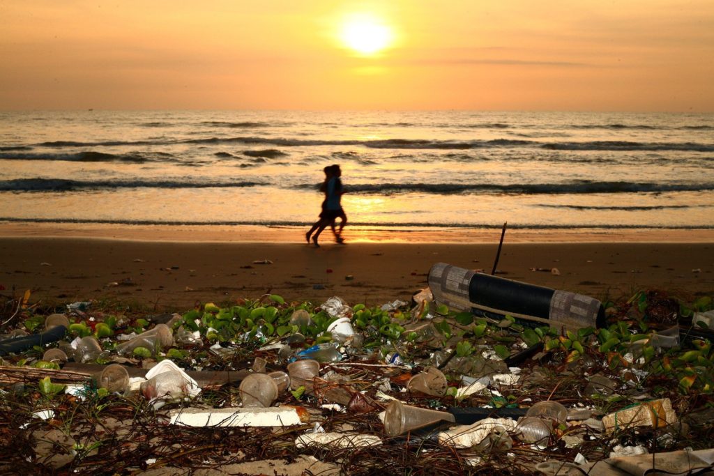 Runners on a beach covered with trash at sunset.