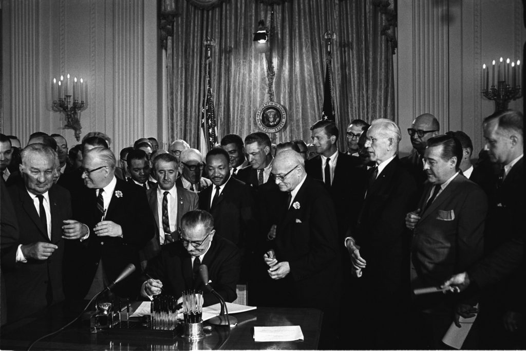 President Lyndon Johnson signs the 1968 Civil Rights Act into law. He is surrounded by Civil Rights activists including Dr. Martin Luther King.