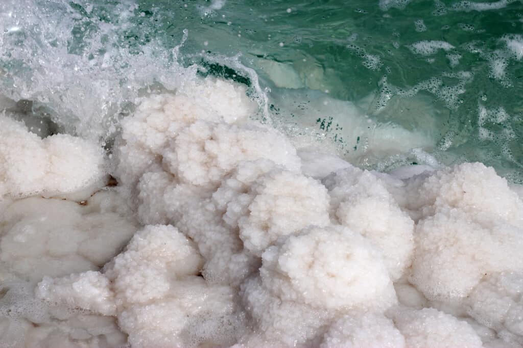 Water splashing as small waves hit the salt crystals covering the shoreline at the Dead Sea scaled