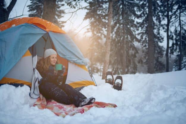 Woman having coffe by tent during winter camping